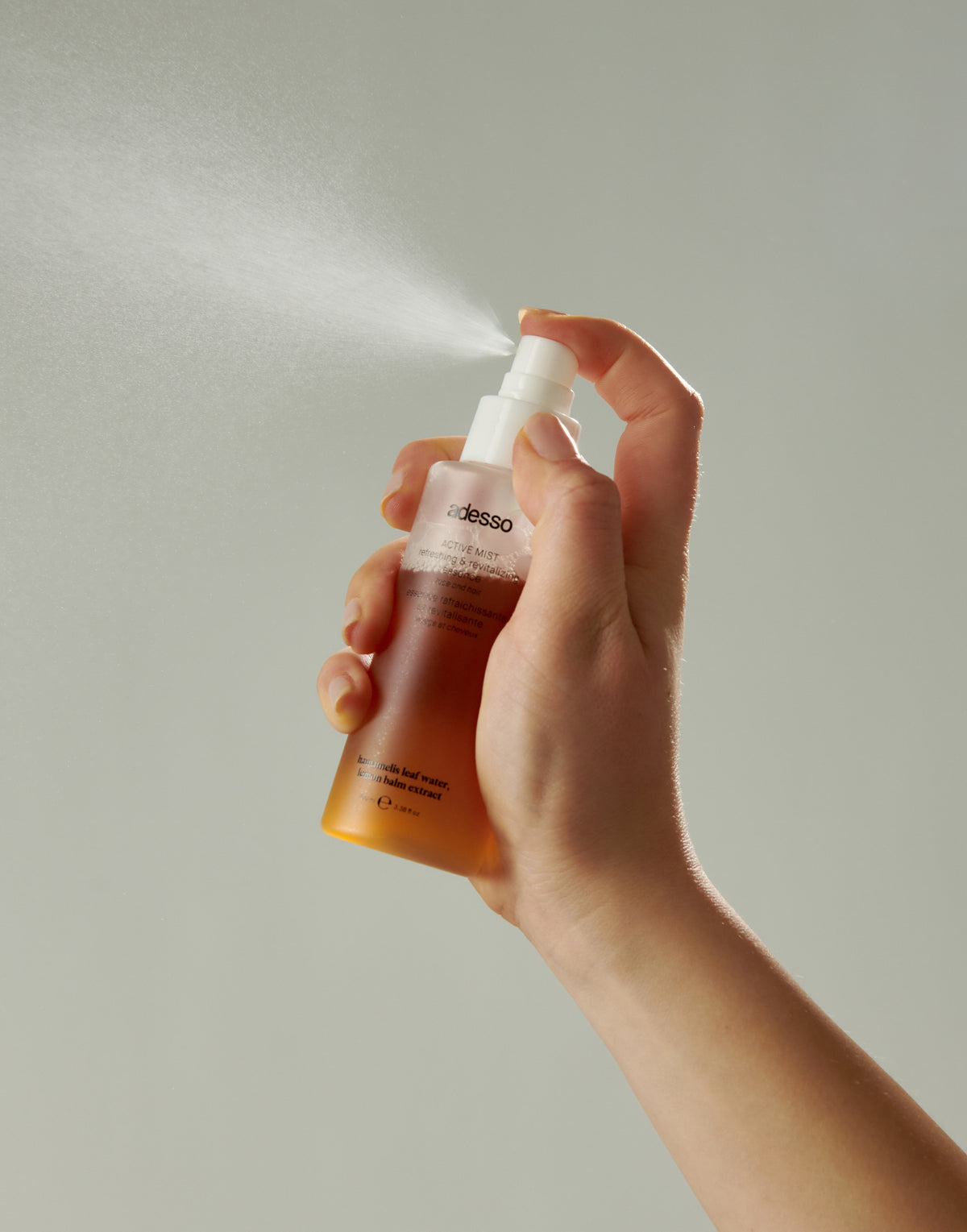 A hand spraying an Adesso skincare product 