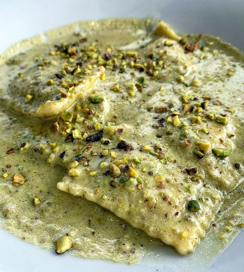 A bowl of ravioli with a pistachio based sauce. 
