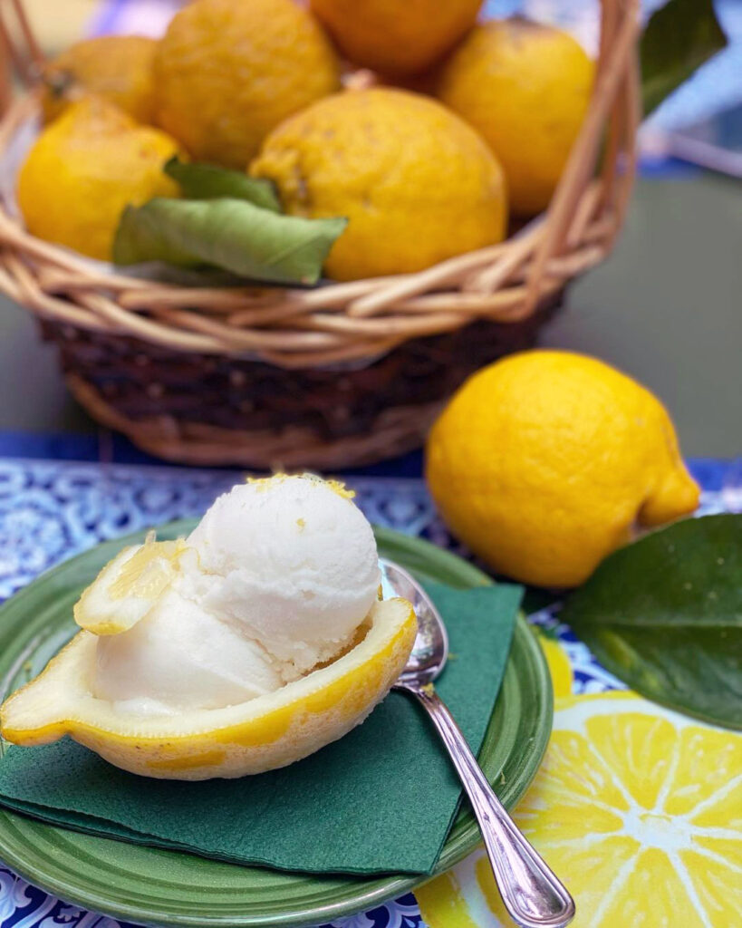 An iced sorbet in a frozen lemon next to a basket of ripe lemons on a table 