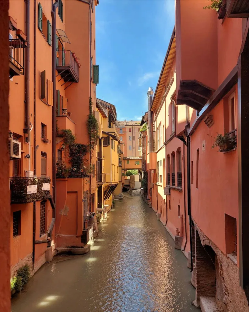The view from the famous "little window" in Bologna, a canal flowing past colorful buildings on a sunny day. 