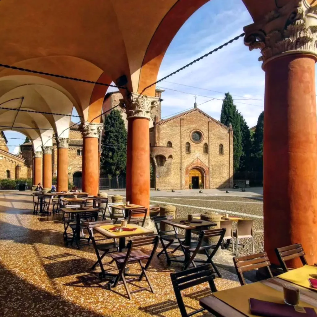 A view of the Seven Churches of Bologna from under the portico next to small outdoor tables. 